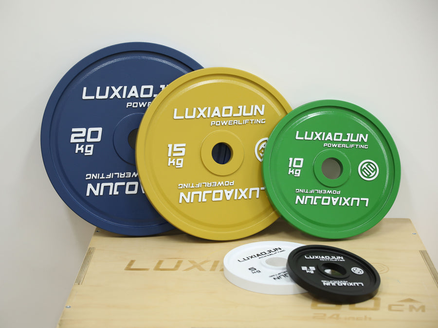 Blue 20 kg, yellow 15 kg, green 10 kg, white 5 kg and black 2.5 kg LUXIAOJUN powerlifting plates arranged by size against a wooden box